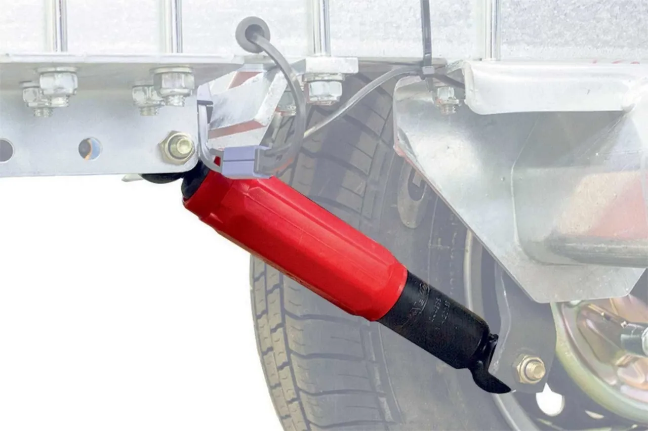 Czerwony amortyzator zamontowany do przyczepki. Pokazuje, jak zamontować amortyzatory do przyczepki, zapewniając płynniejszą jazdę.