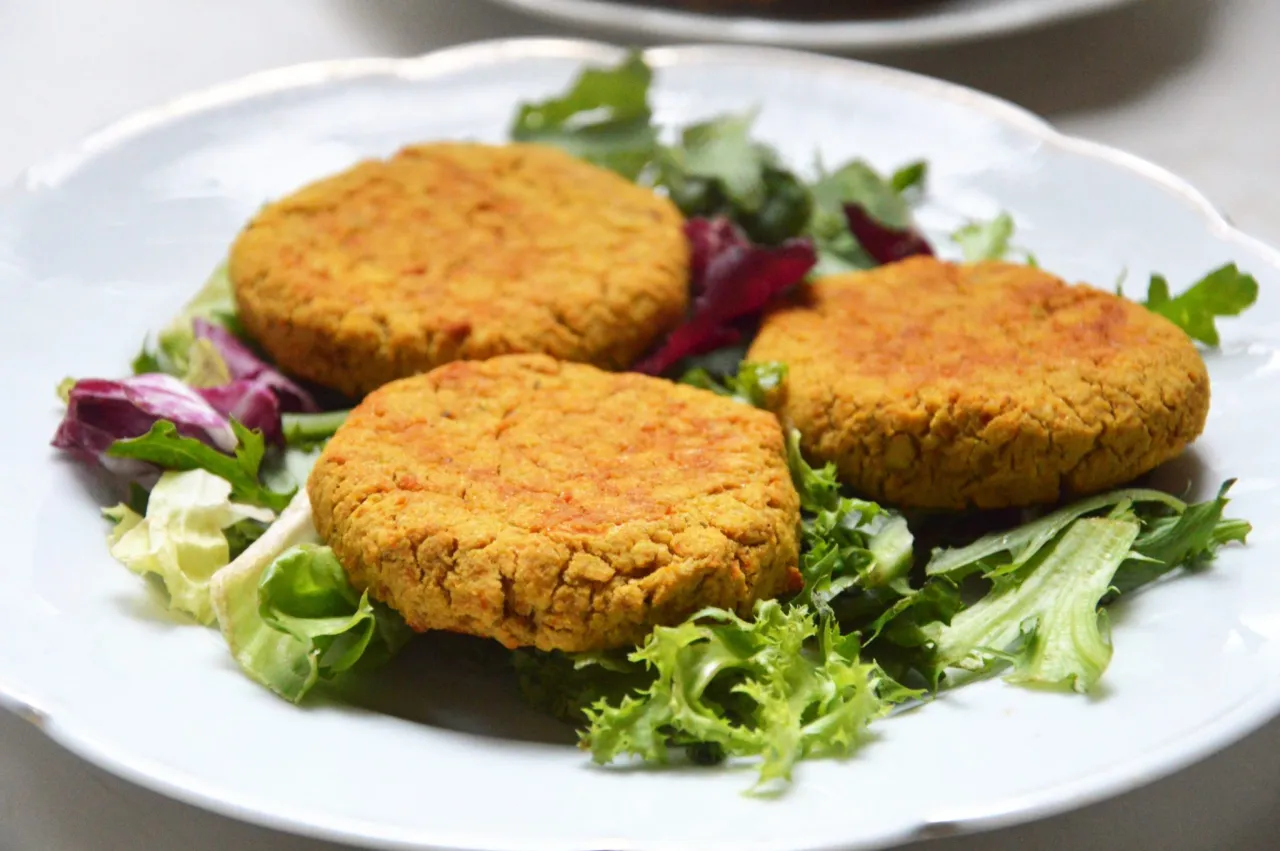 Trzy złociste kotleciki z ciecierzycy na talerzu z sałatką. Idealne co na obiad zamiast ryby, gdy masz ochotę na coś pysznego i zdrowego.