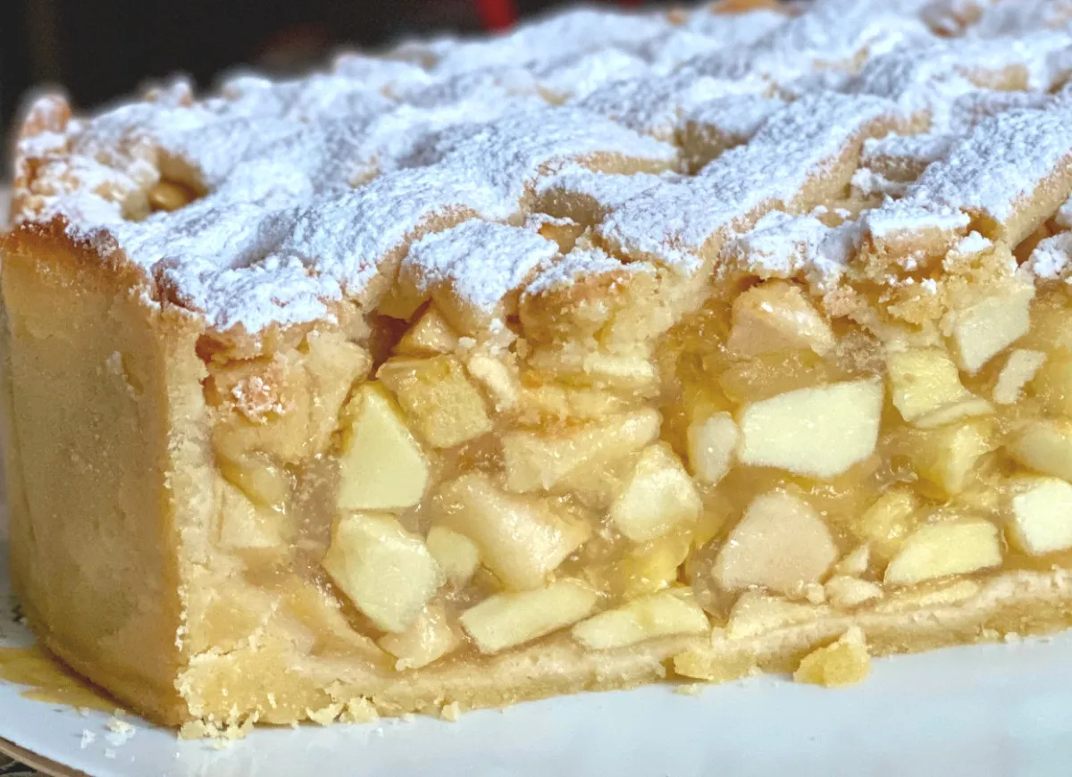 Szarlotka z widocznymi kawałkami jabłek, posypana cukrem pudrem. Chcesz wiedzieć, co zrobić, żeby jabłka w szarlotce były sztywne?