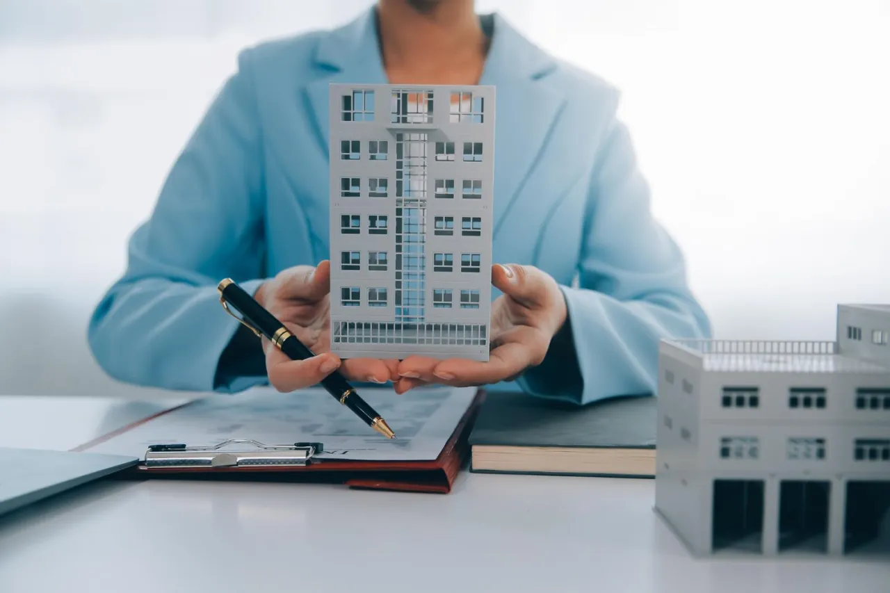 Pośrednik nieruchomości prezentuje model budynku, symbolizując ubezpieczenie inwestycji.