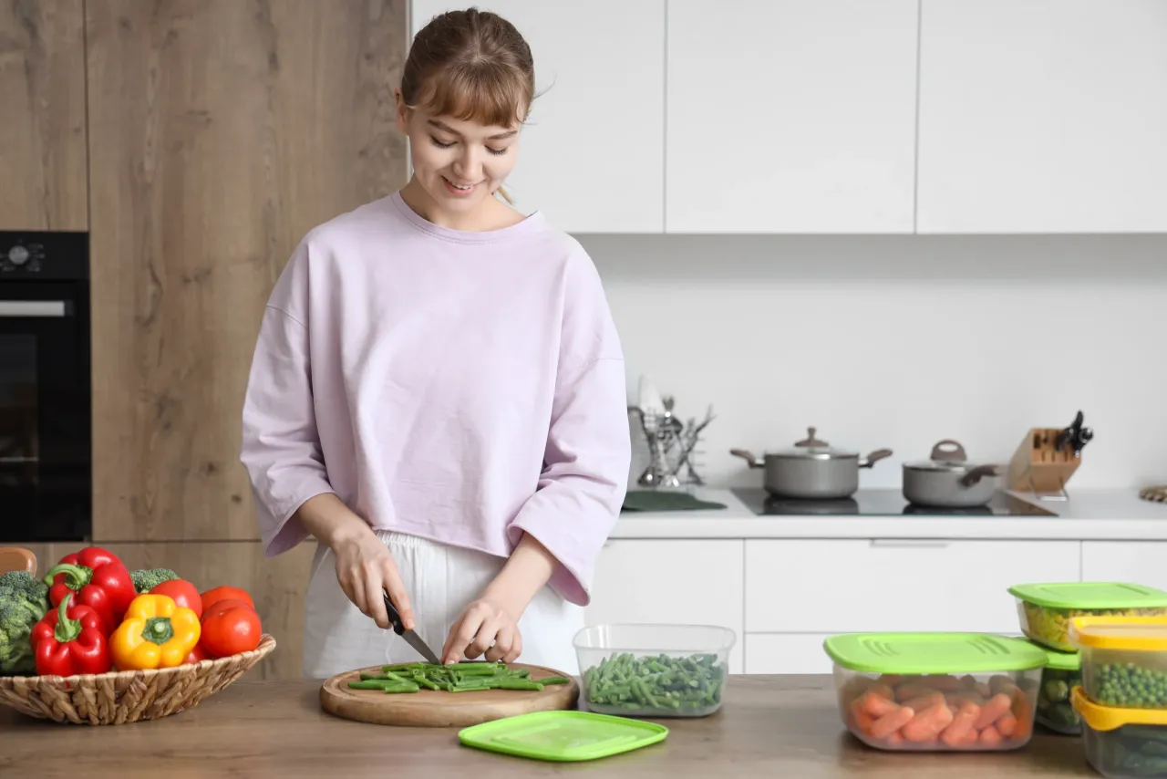 Młoda kobieta kroi fasolkę szparagową, przygotowując posiłek. To przykład, co to jest kuchnia wegańska &ndash; pełna świeżych warzyw i zdrowych składnik&oacute;w.