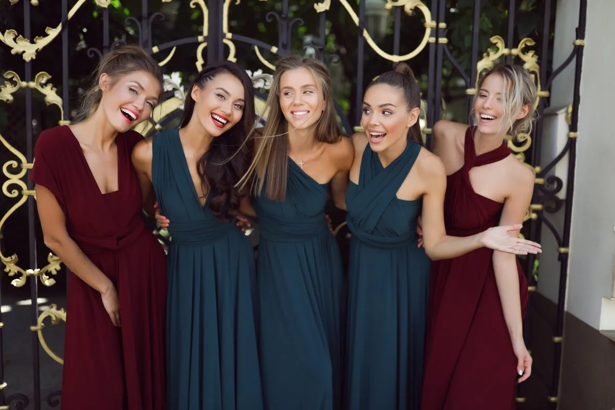 Pięć uśmiechniętych kobiet w pięknych sukniach, tworzących idealną świadkową stylizację. Dwie w bordowych, trzy w butelkowozielonych.