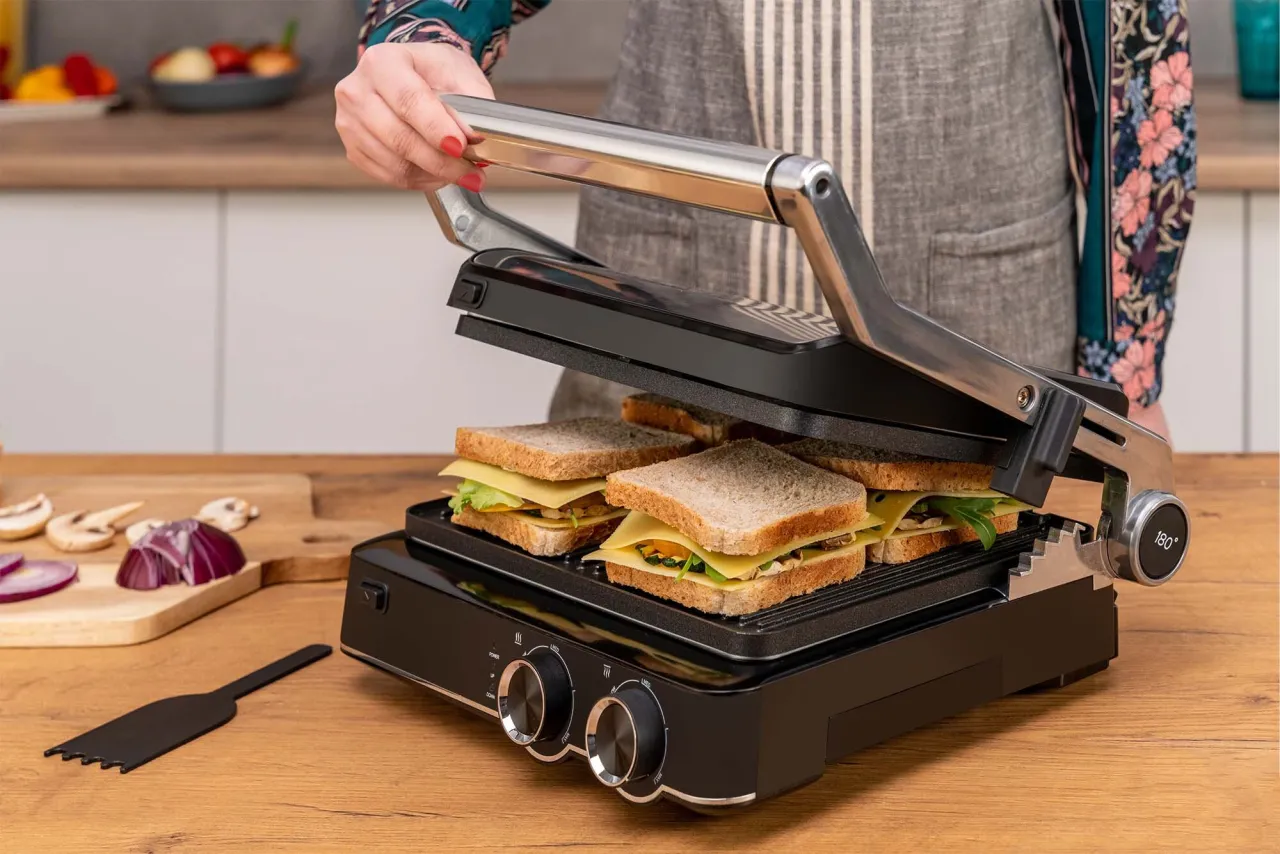 Grill elektryczny Götze & Jensen GL802X przygotowuje pyszne tosty. Na płycie grilla leżą cztery kanapki z serem i warzywami.