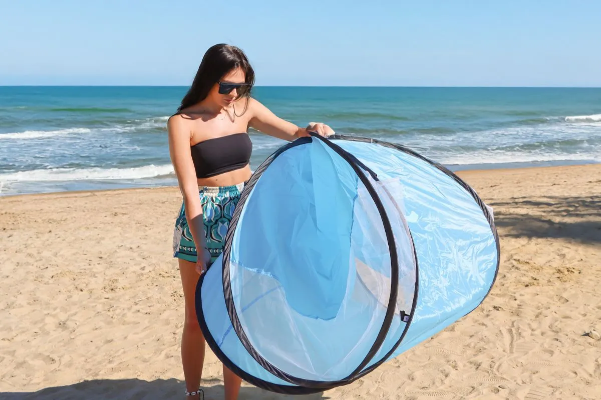 Kobieta na plaży trzyma niebieski namiot samorozkładający. Pokazuje, jak złożyć namiot samorozkładający, by łatwo go schować.