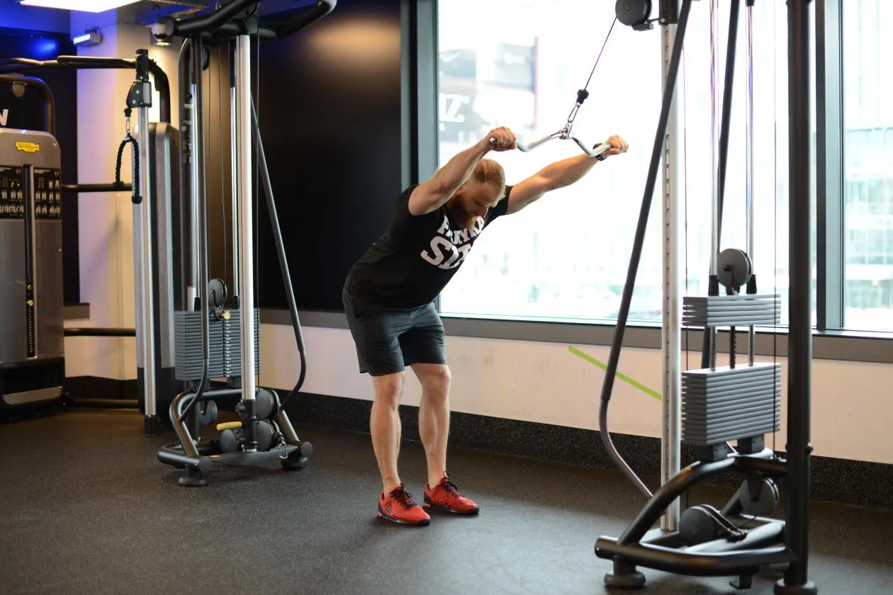 Mężczyzna wykonuje ćwiczenia na wyciągu g&oacute;rnym, trenując ramiona.