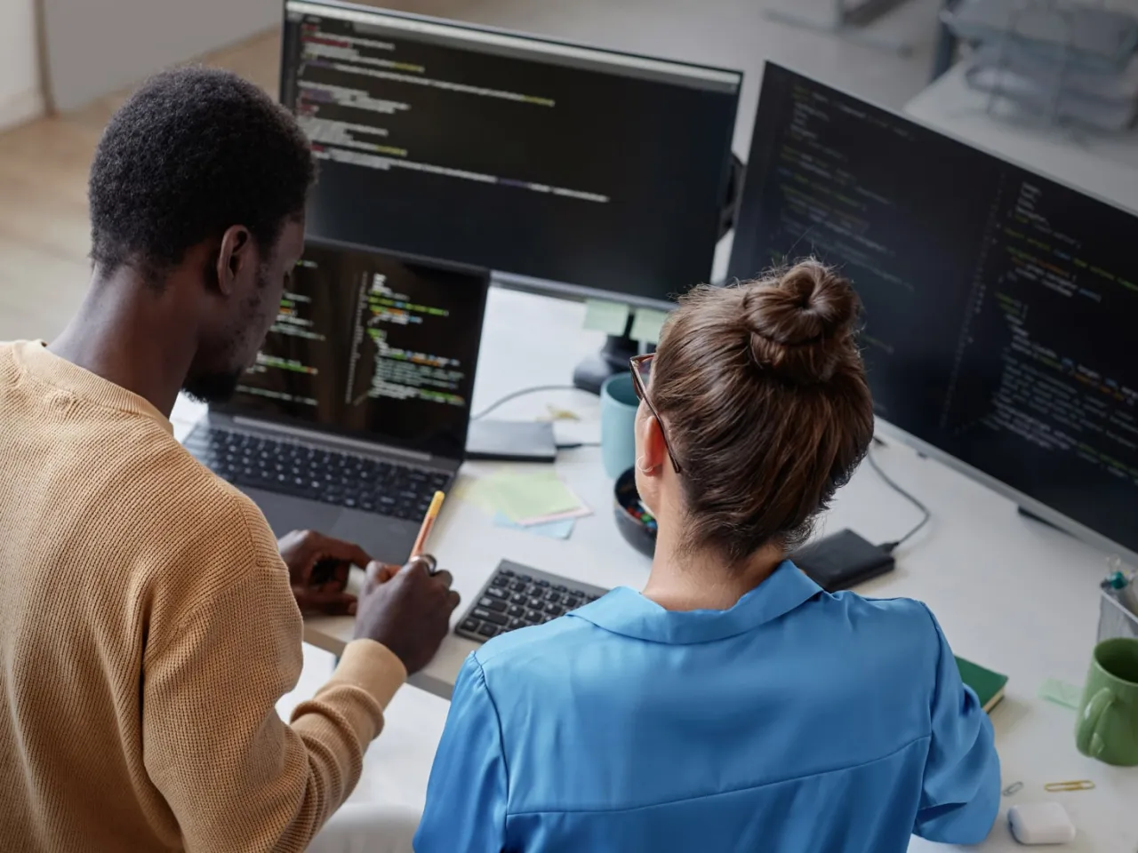 Dwóch programistów pracuje nad kodem, jeden pisze skrypt, drugi analizuje. W tle widać monitory z kodem, być może do export bash.