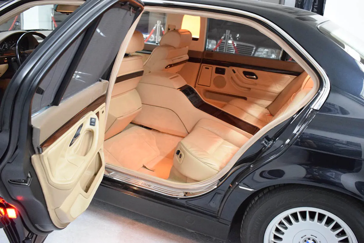 Wnętrze luksusowego BMW E38 Long z jasną tapicerką i drewnianymi wstawkami. Widok na tylne siedzenia i drzwi.