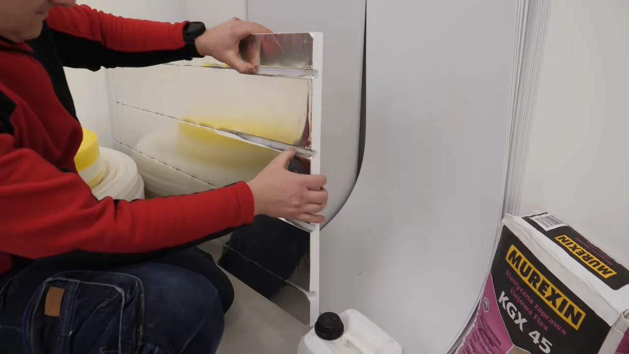 Montaż ogrzewania podłogowego bez wylewki. Ręce układają izolację z folii aluminiowej na płycie.