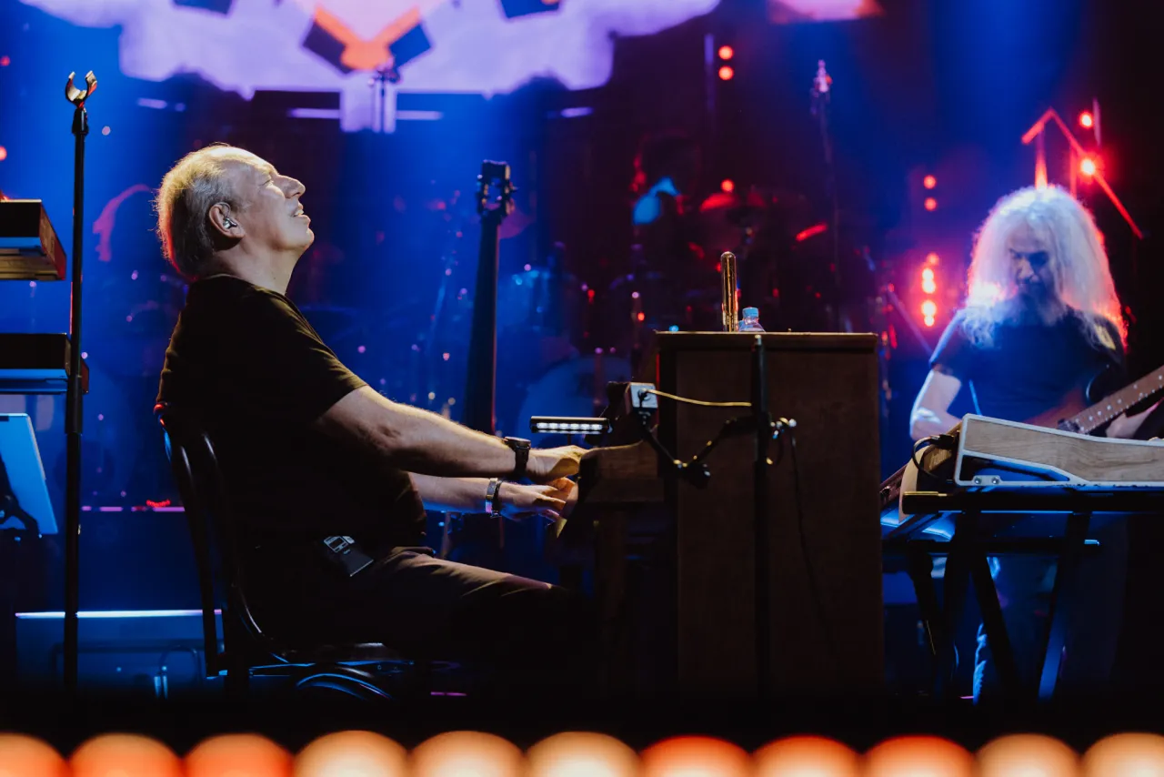 Hans Zimmer gra na pianinie, a jego zesp&oacute;ł towarzyszy mu na scenie. Koncert trwa, a widzowie są zachwyceni.