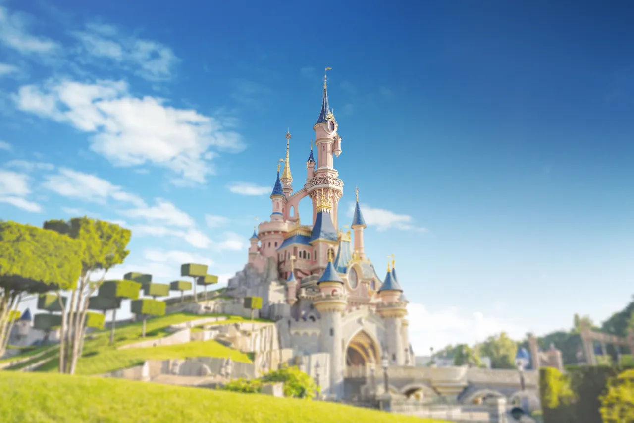 Bajkowy zamek w Disneylandzie Paryż, jedna z głównych atrakcji, na tle błękitnego nieba z chmurami.