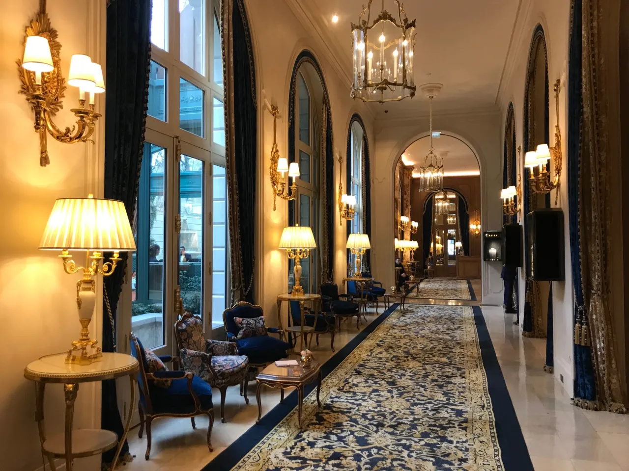 Elegancki korytarz hotelu Ritz w Paryżu, z luksusowym dywanem, złotymi lampami i zabytkowymi meblami.
