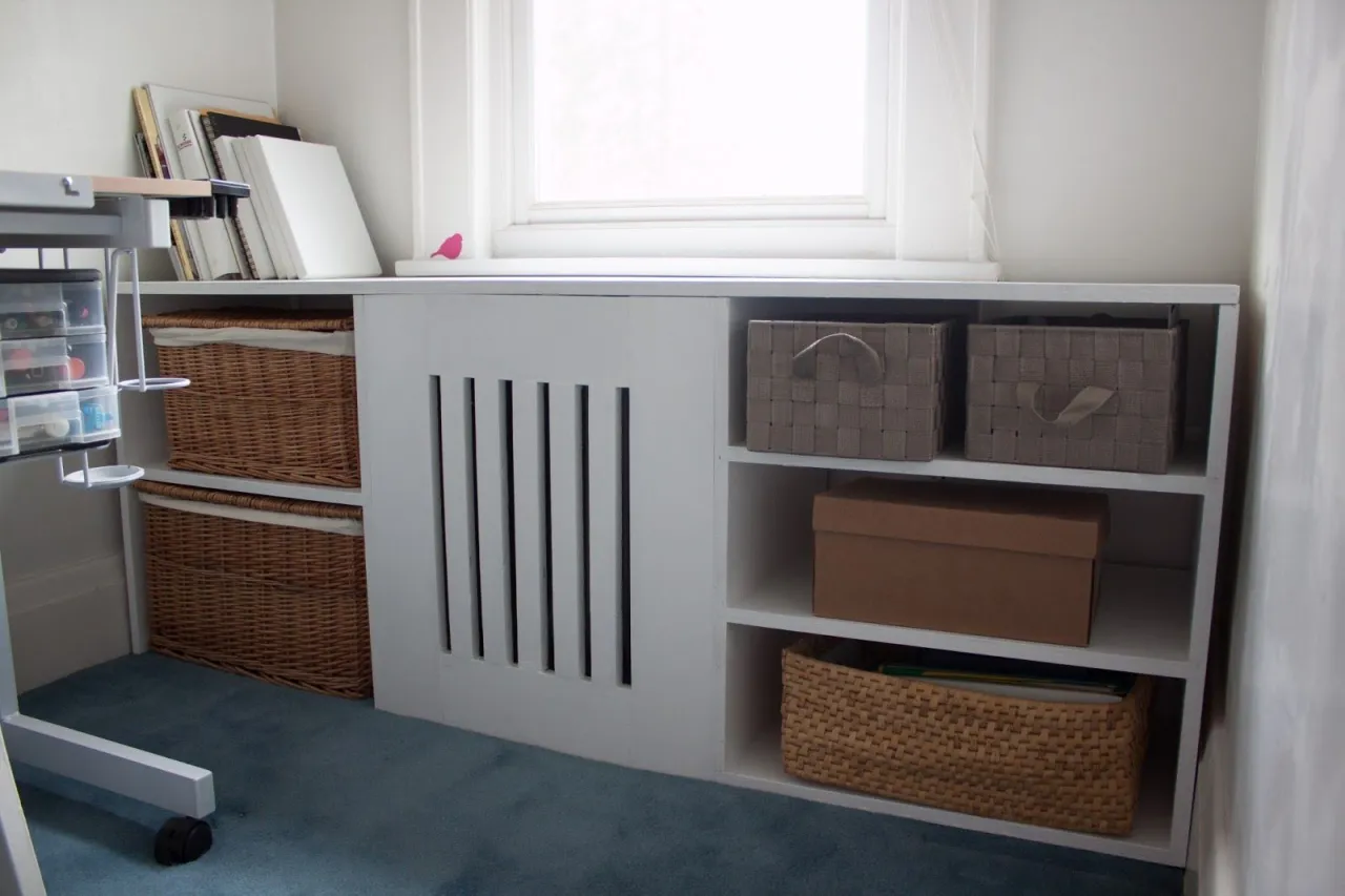 Pomysł, jak ukryć grzejnik: biała zabudowa z p&oacute;łkami i koszami, idealna do przechowywania.