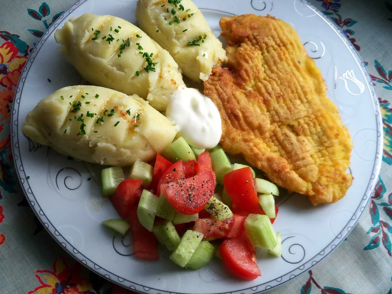 Złocisty kotlet schabowy, ziemniaki puree z koperkiem i świeża sałatka z pomidorów i ogórków – idealne połączenie, które pasuje do schabowego.