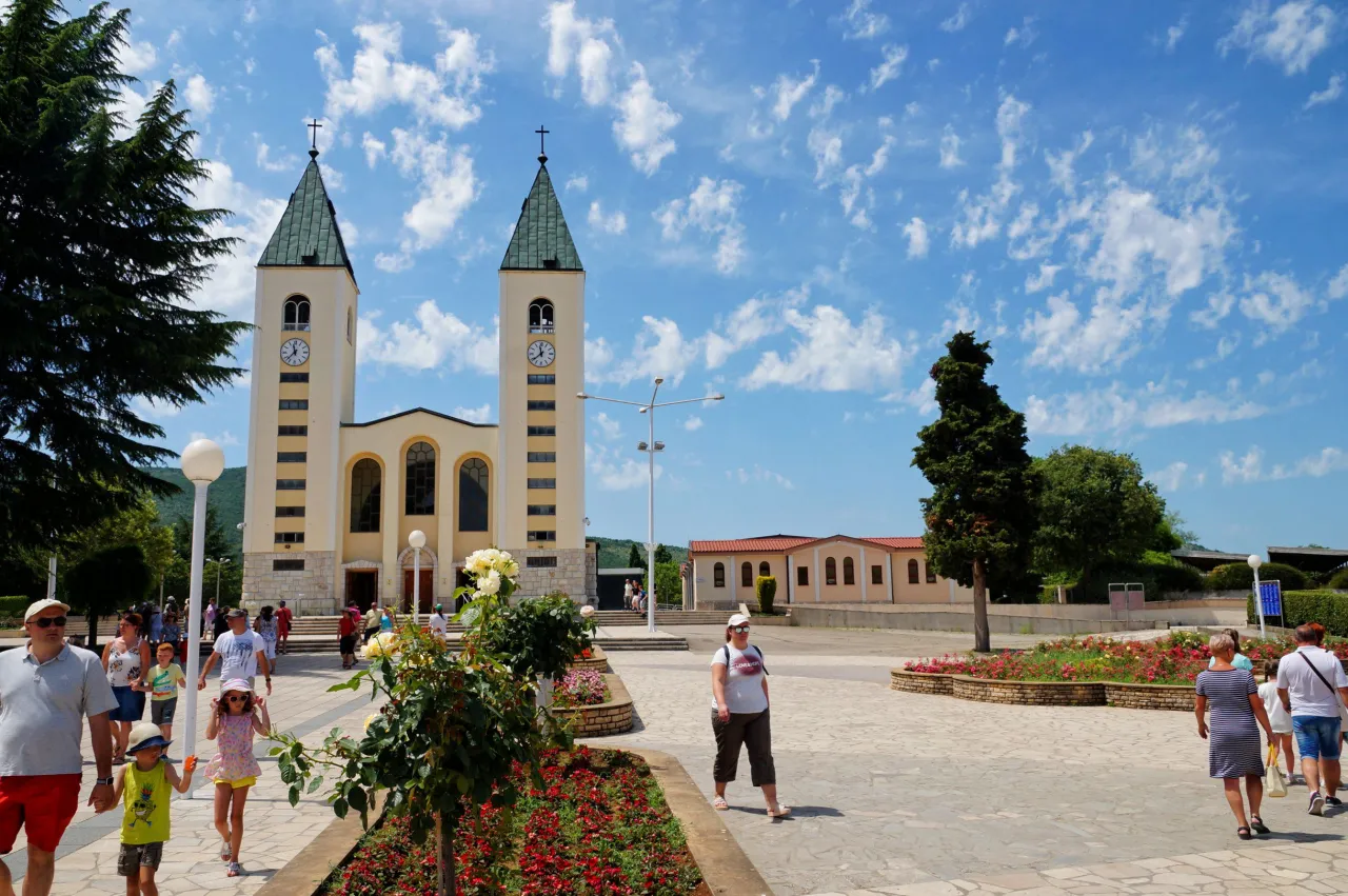 Ludzie spacerują po placu przed kościołem w Medziugorie. W tle widać charakterystyczne wieże. Czy w Medziugorie jest bezpiecznie? Wygląda na spokojne miejsce.