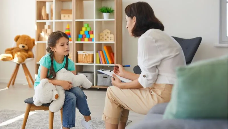 terapeuta logopeda bawi się z dzieckiem z autyzmem na dywanie