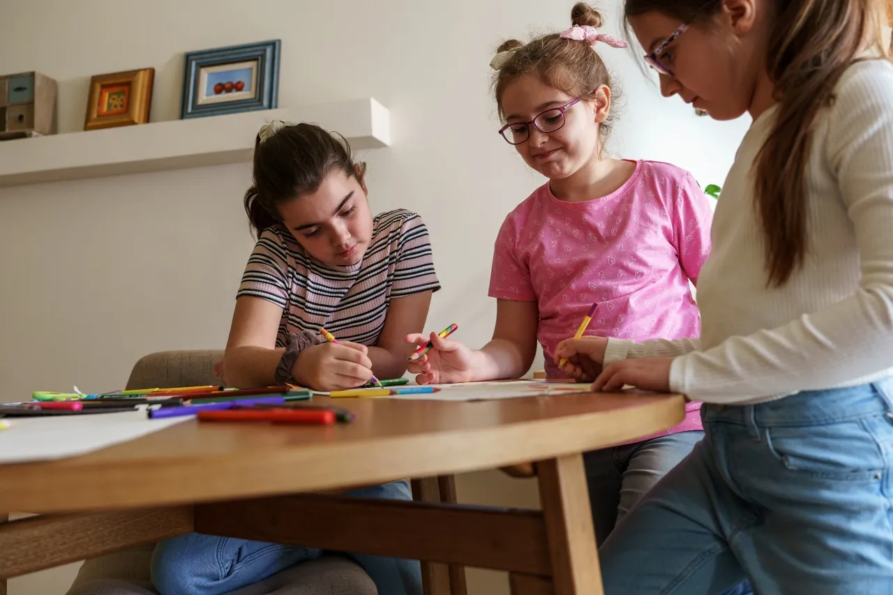 Trzy dziewczynki rysują przy stole. Widać, jak wygląda nauczanie indywidualne – każda skupiona na swoim zadaniu, ale w bliskim kontakcie.