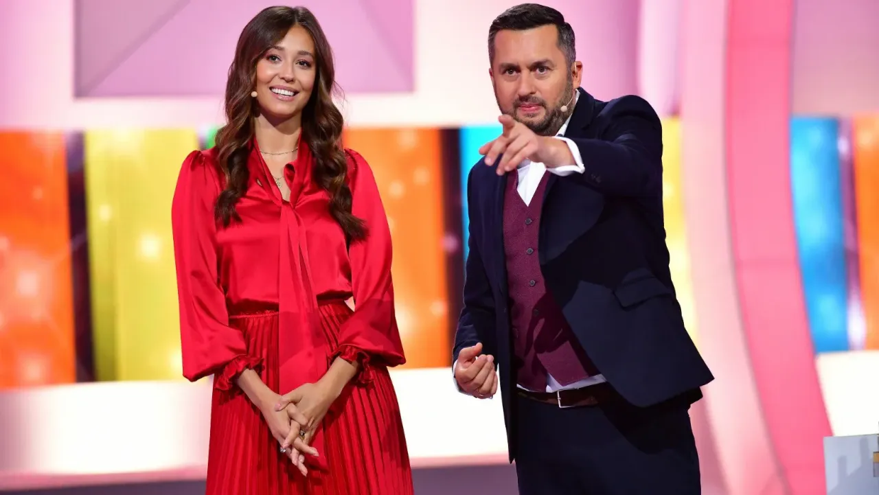 Kto prowadzi Koło Fortuny z Brzozowskim? Uśmiechnięta prezenterka w czerwonej sukni i prowadzący, który wskazuje palcem.