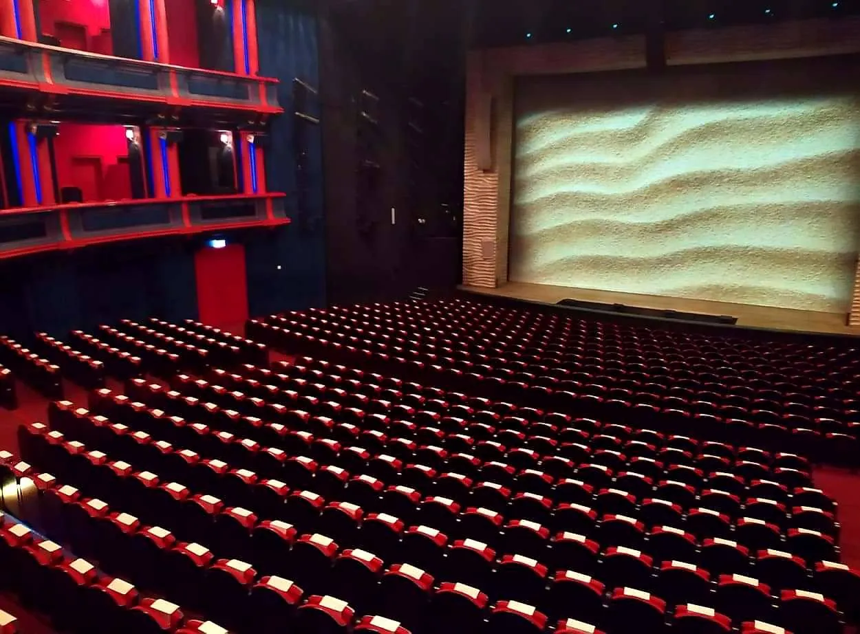 Puste rzędy czerwonych foteli w teatrze czekają na widzów. Scena z piaskowym tłem sugeruje, ile jest miejsc w teatrze Roma.