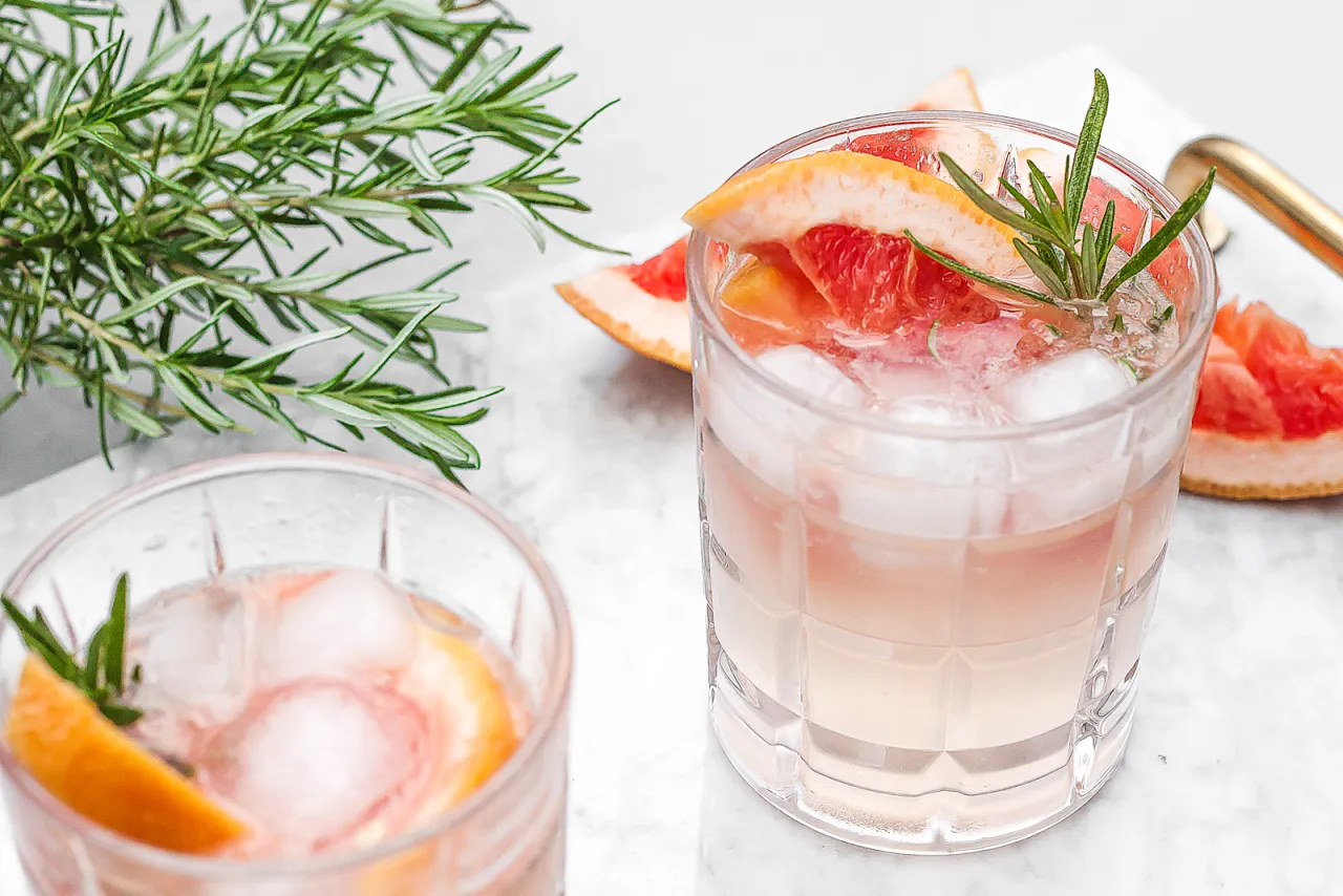 Dwa orzeźwiające drinki: gin z tonikiem i gin z różową lemoniadą, ozdobione grejpfrutem i rozmarynem.