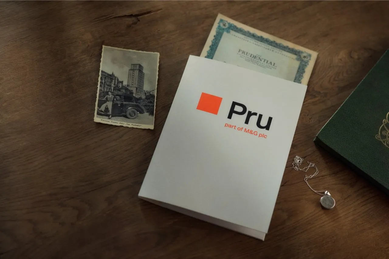 Prudential co to za firma? Na zdjęciu: stara poczt&oacute;wka z budynkiem Prudential w Warszawie, dokument z logo Prudential, broszura Pru i naszyjnik.