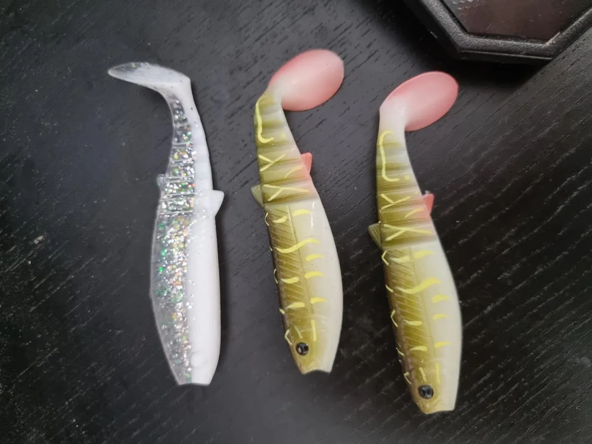 Trzy gumowe przynęty wędkarskie: jedna srebrna brokatowa, dwie imitujące ukleję. Idealne na to, na co biorą ryby.