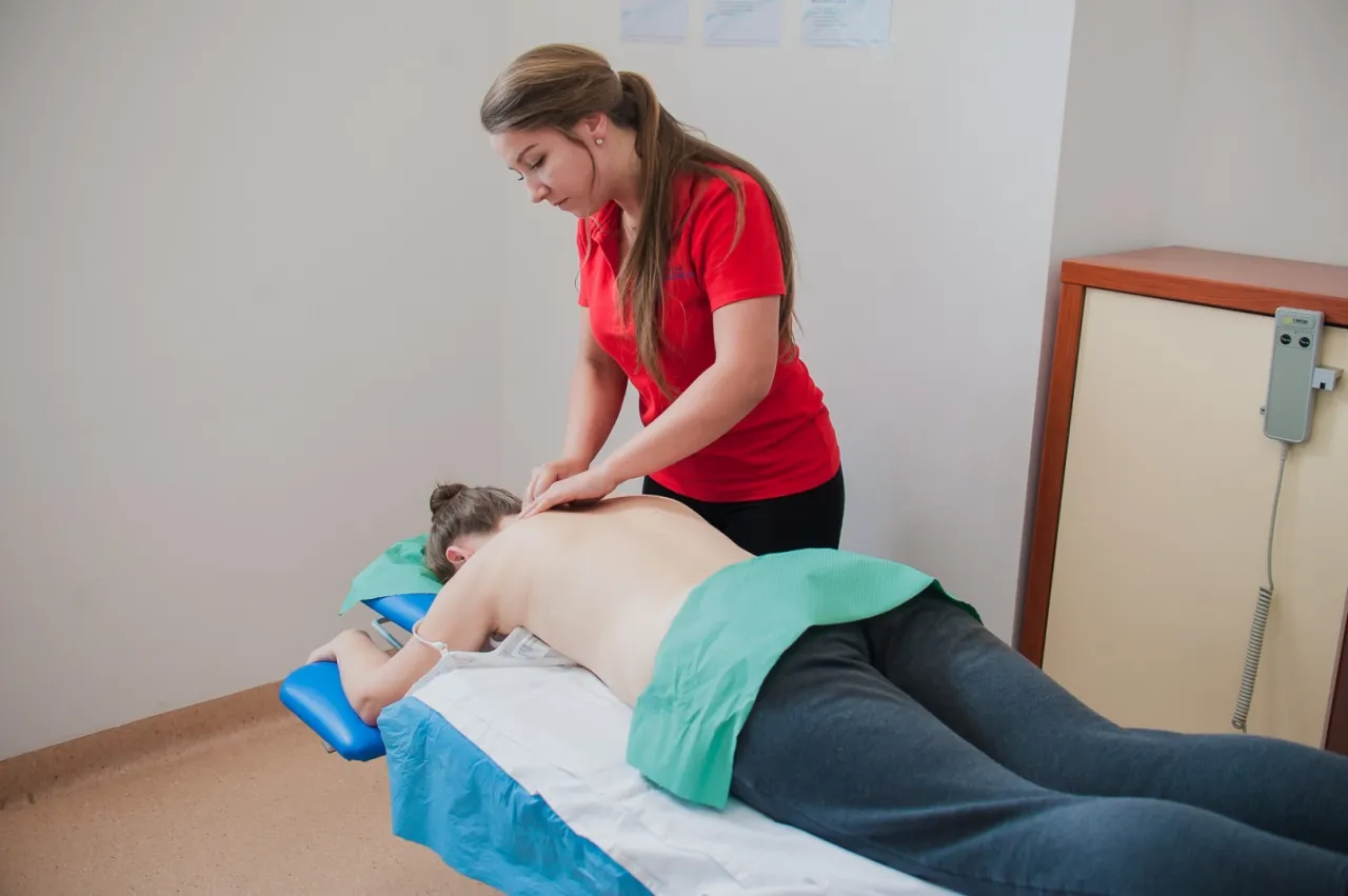Fizjoterapeuta wykonuje masaż pleców pacjentowi leżącemu na kozetce.