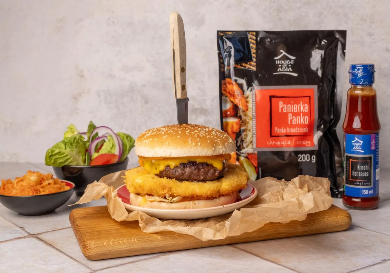 Burger z chrupiącą panierką panko i sosem kimchi. Obok miseczka z kimchi i sałatka. Idealne połączenie smak&oacute;w!
