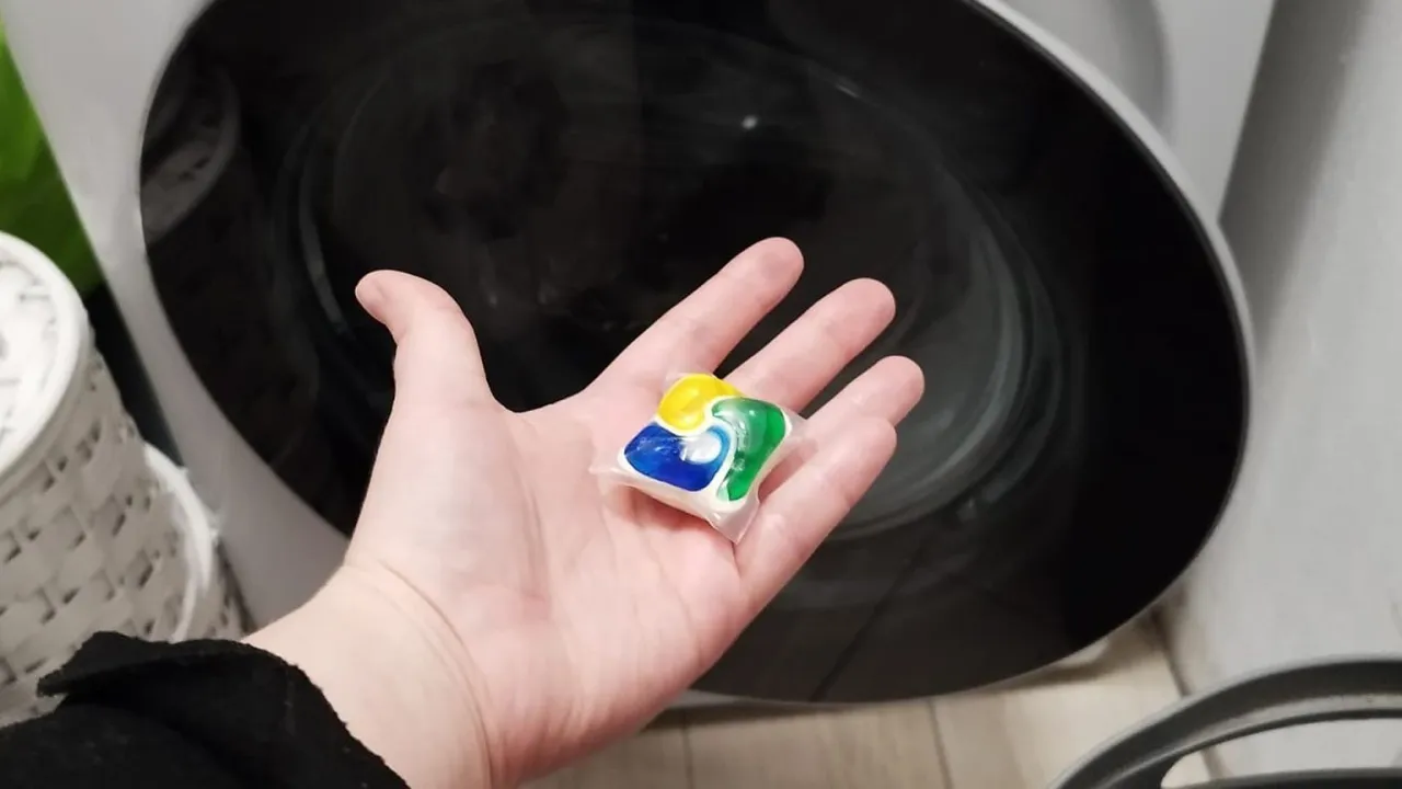 Dłoń trzyma kapsułkę do zmywarki, zastanawiając się, czy czyszczenie pralki tabletkami do zmywarki faktycznie niszczy uszczelki.