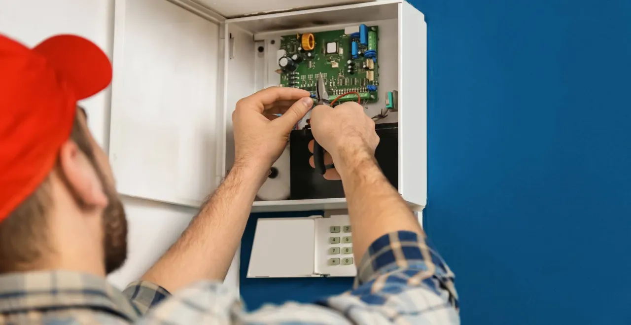 Technik podłącza jaki kabel do alarmu w domu, pracując przy centralce i klawiaturze.