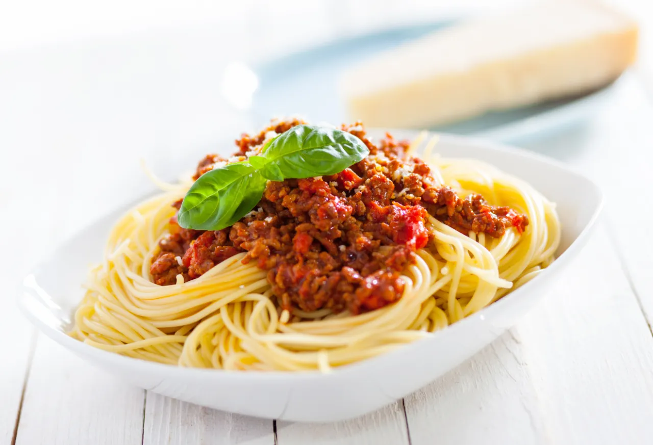 Klassische Spaghetti Bolognese in einer tiefen wei&szlig;en Sch&uuml;ssel, garniert mit Basilikum