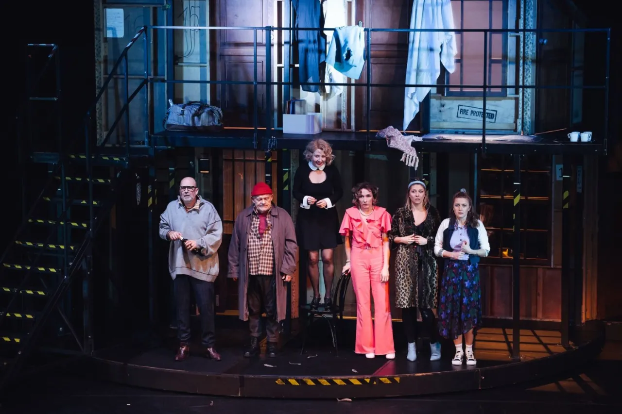 Aktorzy na scenie, w r&oacute;żnorodnych strojach, tworzą atmosferę tajemnicy. O co biega spektakl? Widzowie zastanawiają się, co wydarzy się dalej.