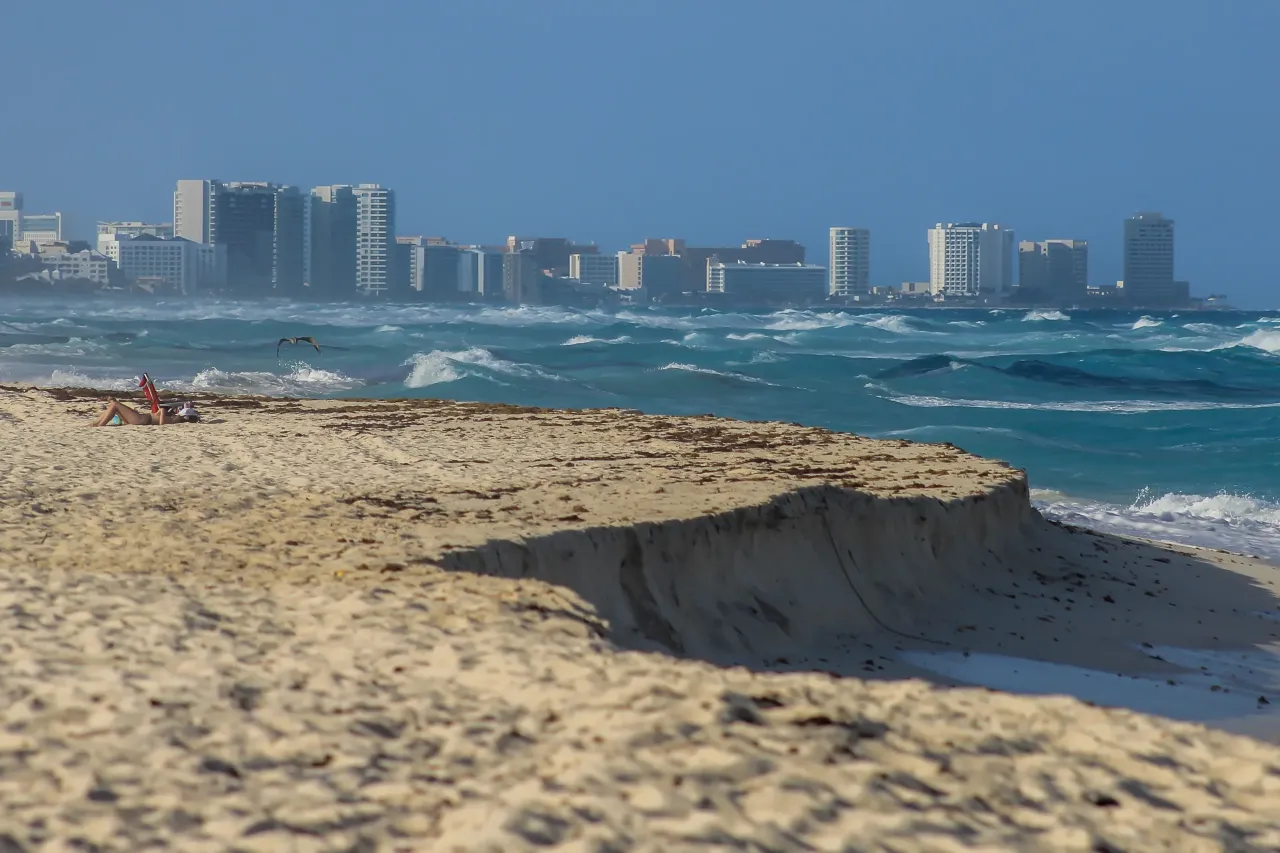 Piękna plaża w Cancun, z falami i hotelami w tle. Czy w Cancun jest bezpiecznie? Tak, turyści cieszą się słońcem i morzem.