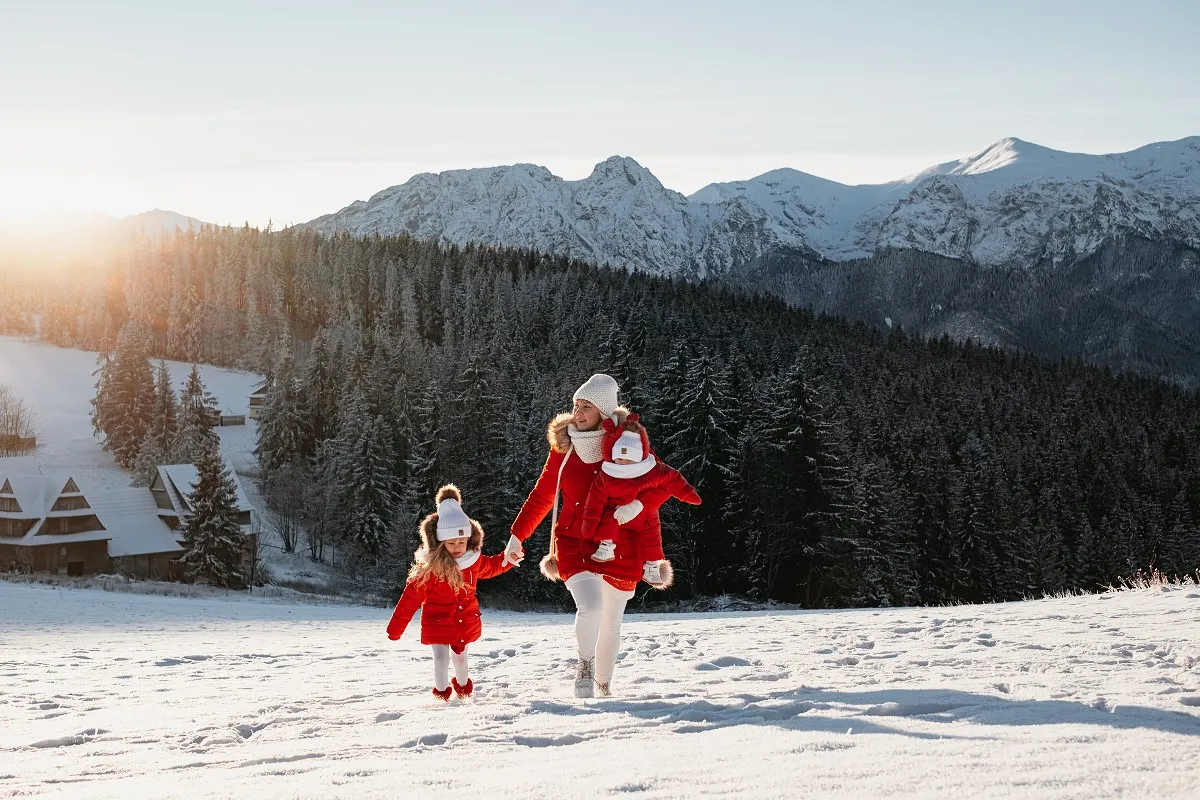 Rodzina z dziećmi bawi się na śniegu w g&oacute;rach