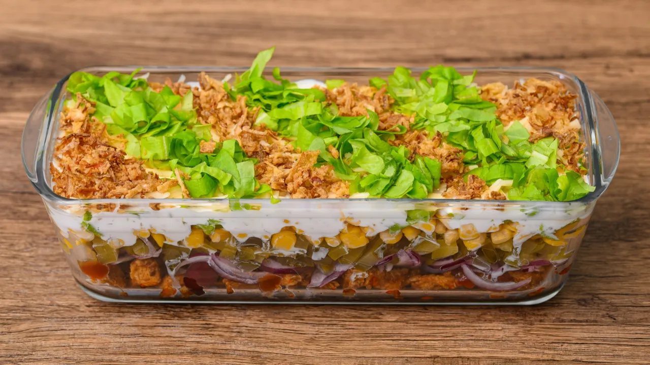 Warstwowa sałatka gyros w szklanym naczyniu, z kurczakiem, kukurydzą, ogórkiem, cebulą i chrupiącą cebulką. Idealna, gdy zastanawiasz się, czy sałatkę gyros można zrobić dzień wcześniej.