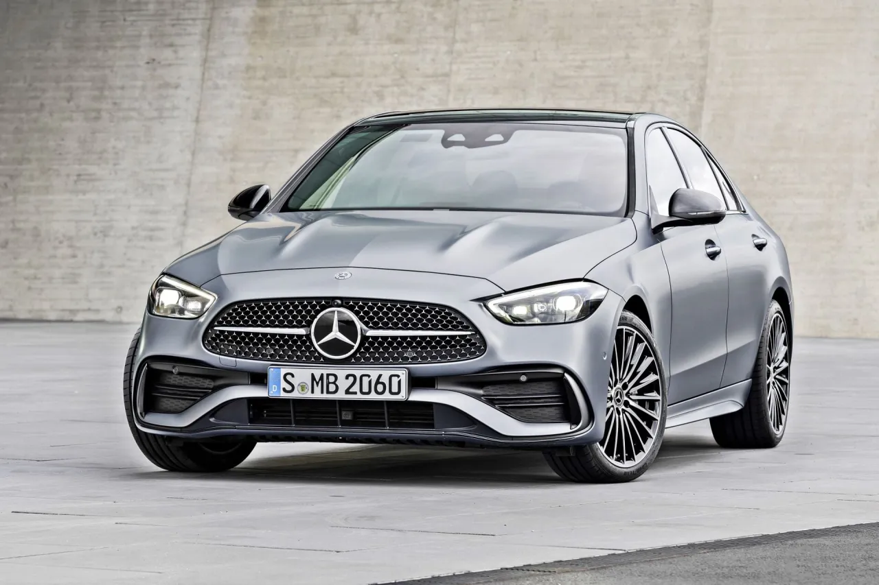 Elegancki, srebrny Mercedes-Benz Klasy C z charakterystyczną atrapą chłodnicy i nowoczesnymi światłami, zaparkowany na tle betonowej ściany.