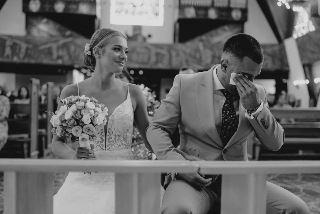 Wzruszony pan młody ociera łzy, panna młoda z bukietem uśmiecha się. Warto wiedzieć, jakie pytania zadać fotografowi ślubnemu, by uchwycił takie emocje.