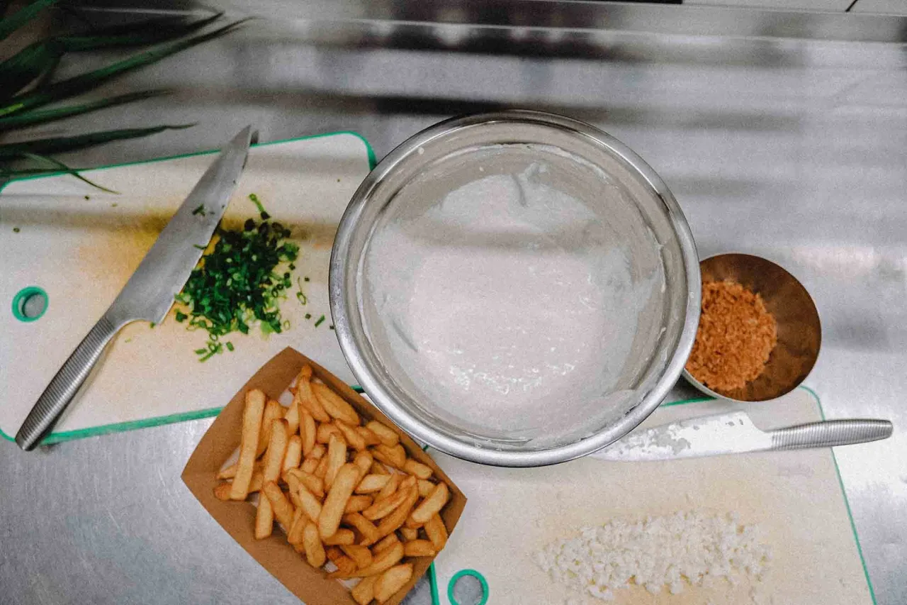 Przygotowania do tego, jak zrobić frytki belgijskie: posiekana cebulka, miska z ciastem, miseczka z przyprawami i gotowe frytki.