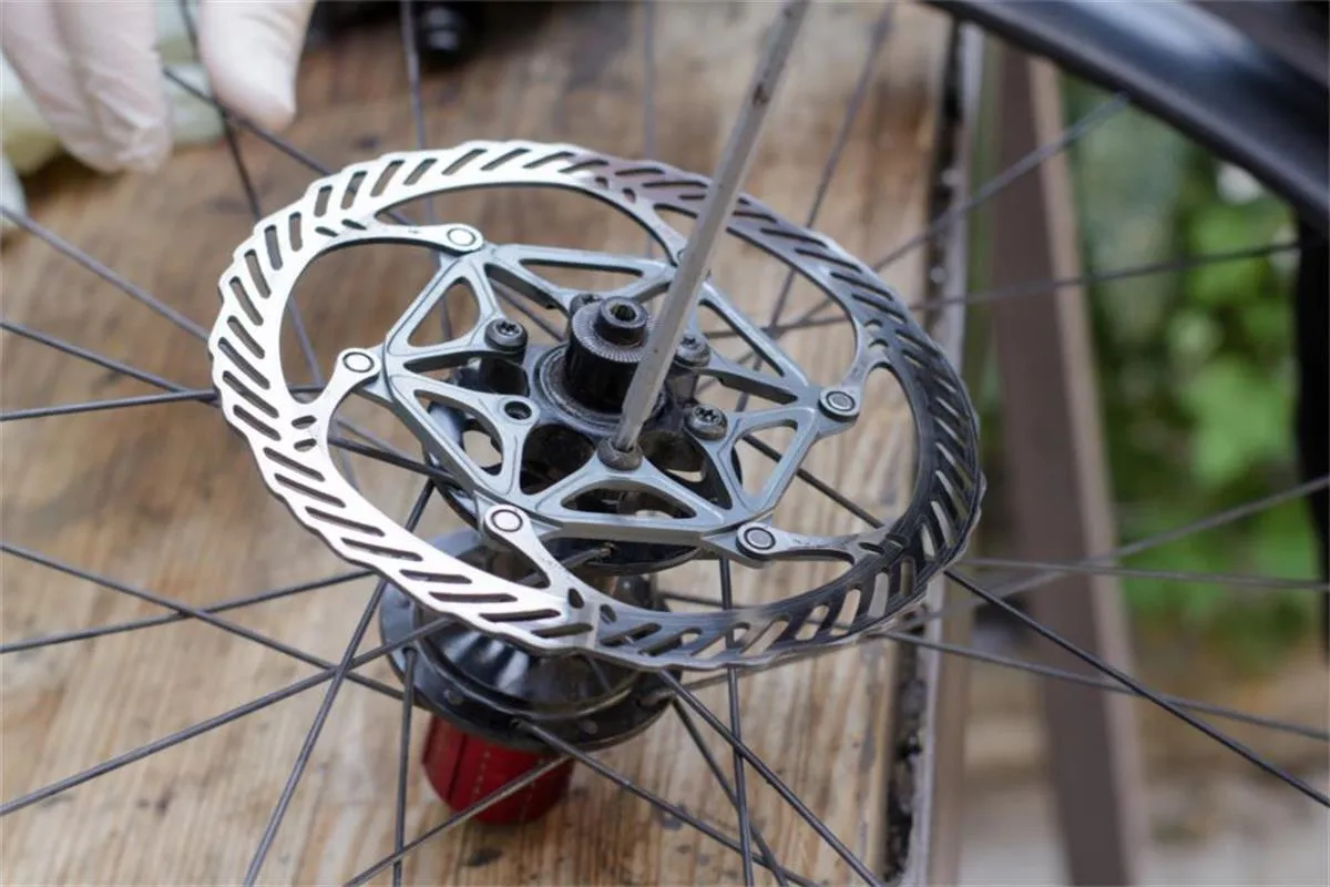 Rowerzysta w białej rękawiczce czyści tarcze hamulcowe. Zastanawiasz się, czym odtłuścić tarcze hamulcowe w rowerze? Zobacz, jak to zrobić!