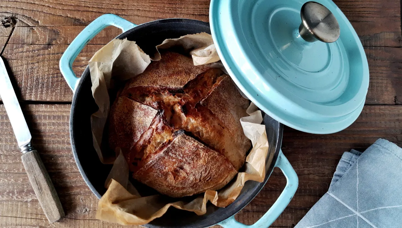 Świeżo upieczony chleb w naczyniu żeliwnym, gotowy do krojenia. Idealny przykład, jak zrobić dobry chleb.