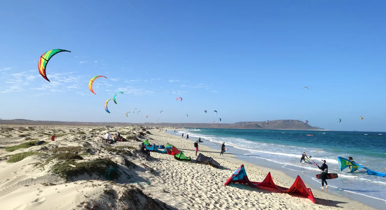 Idealny czas na kitesurfing na Wyspach Zielonego Przylądka to okres od listopada do maja, kiedy wieją silne wiatry. Na plaży widać kolorowe latawce i surferów.
