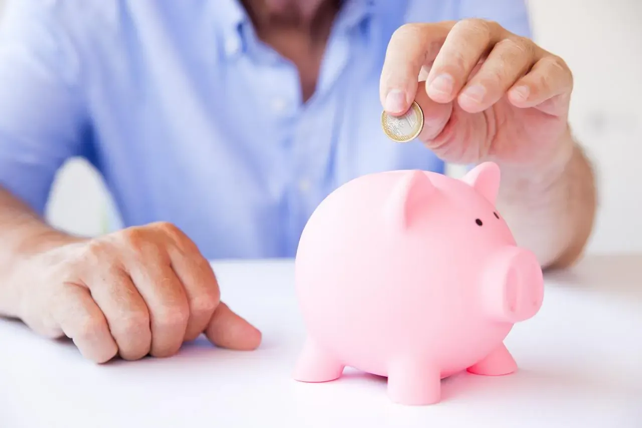 Decyzja między lokaty czy konto oszczędnościowe. Mężczyzna wrzuca monetę do różowej świnki-skarbonki, budując oszczędności.