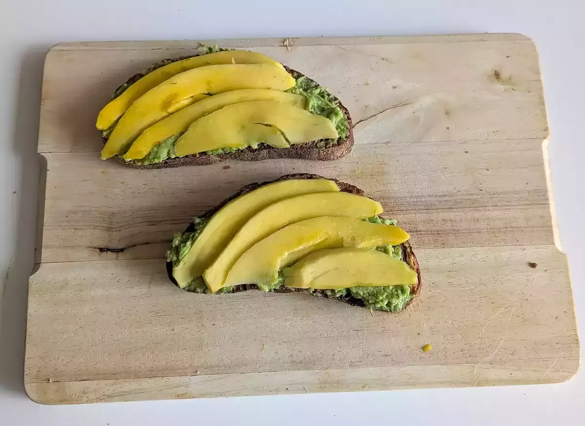 Dwa tosty z pastą z awokado i plasterkami mango. Prosty sposób, jak obierać awokado i przygotować pyszne śniadanie.