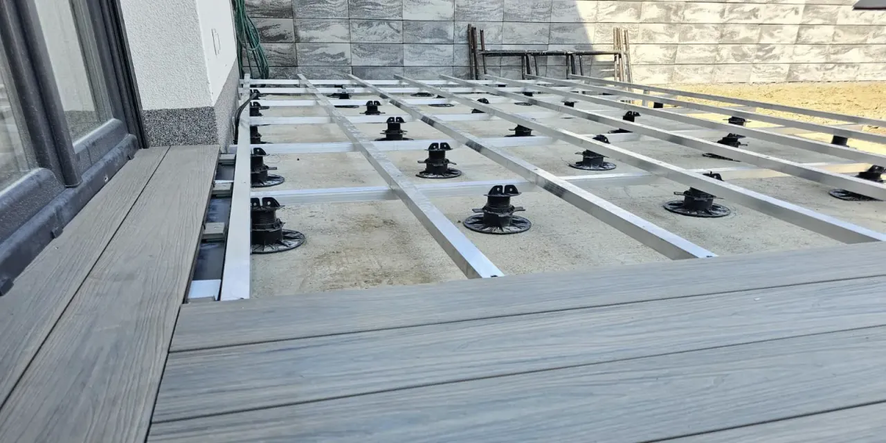 Budowa tarasu z deski kompozytowej: konstrukcja z aluminiowych legarów na regulowanych podporach, gotowa do ułożenia desek.