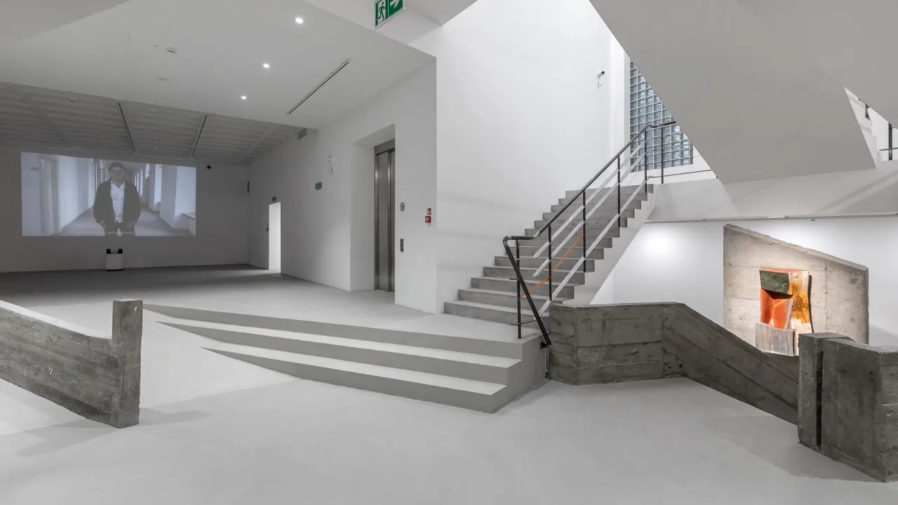 Wnętrze muzeum sztuki wsp&oacute;łczesnej Krak&oacute;w: projekcja wideo, betonowe schody i rzeźba.