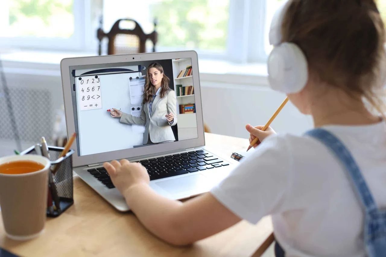 Dziecko w słuchawkach uczy się matematyki przez internet. Nauczycielka tłumaczy liczby na ekranie laptopa, pokazując, co z nauką zdalną.