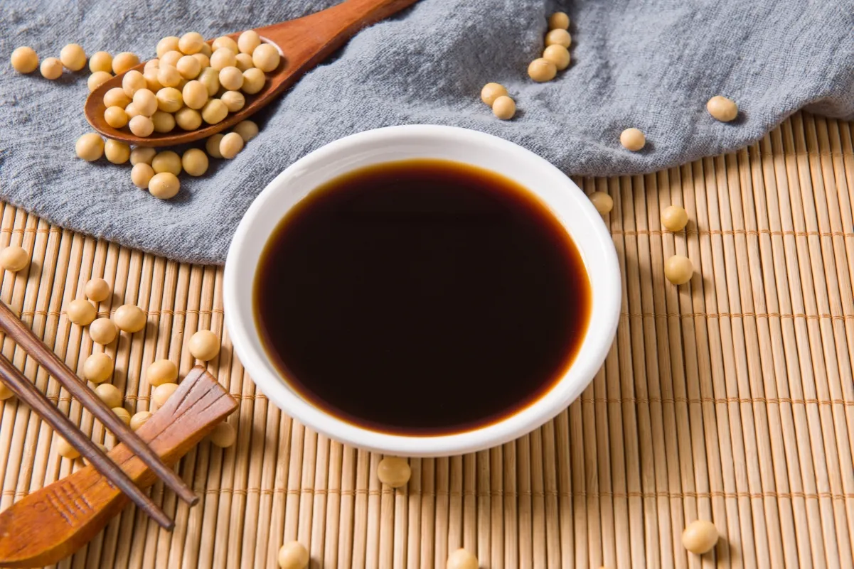 Sos sojowy w miseczce, obok ziaren soi i pałeczek. Idealny dodatek do wielu dań azjatyckich.