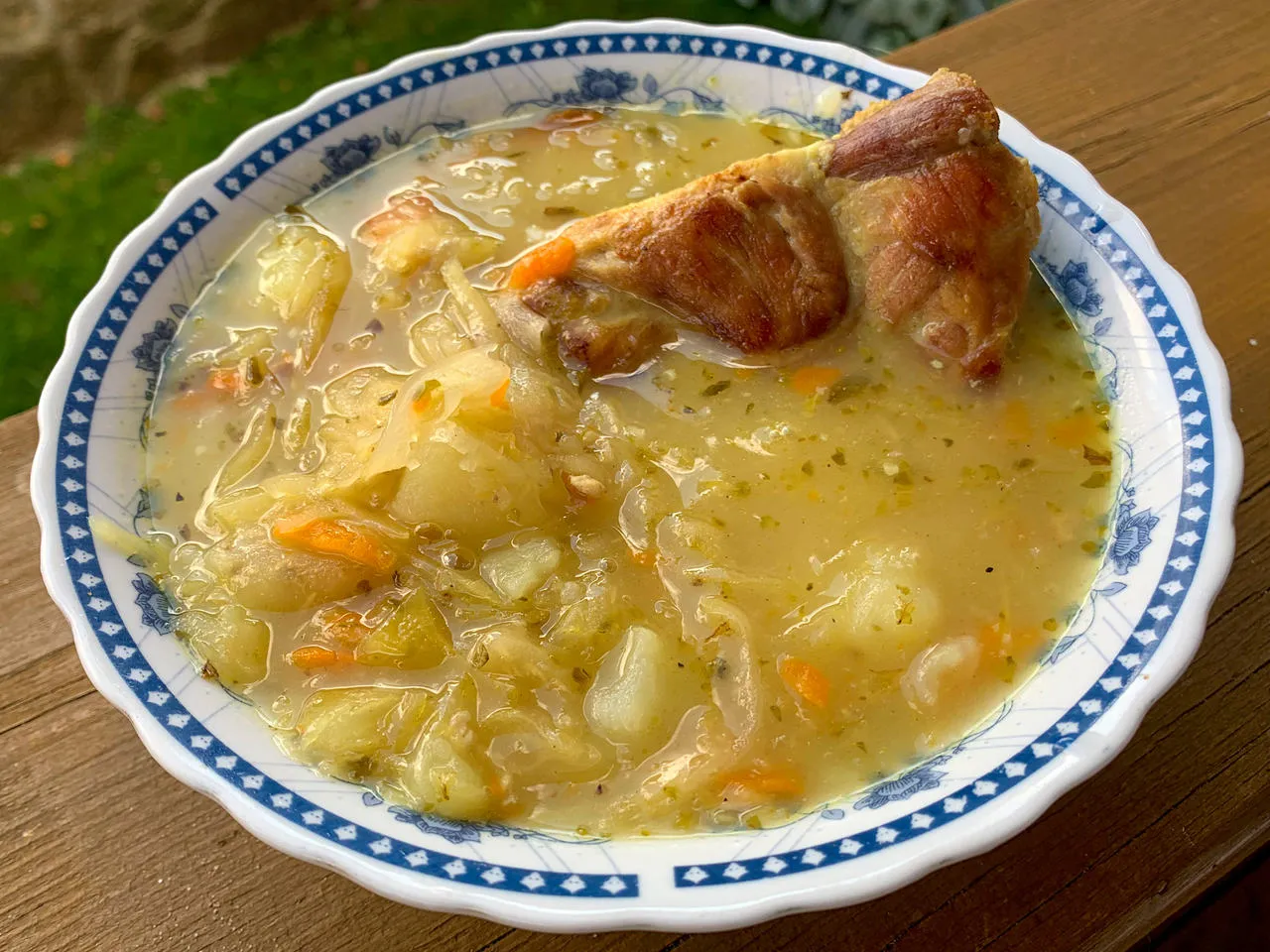 Kapuśniak ze świeżej kapusty czy kwaśnica? Aromatyczna zupa z kawałkiem mięsa, ziemniakami i marchewką w misce z niebieskim wzorem.