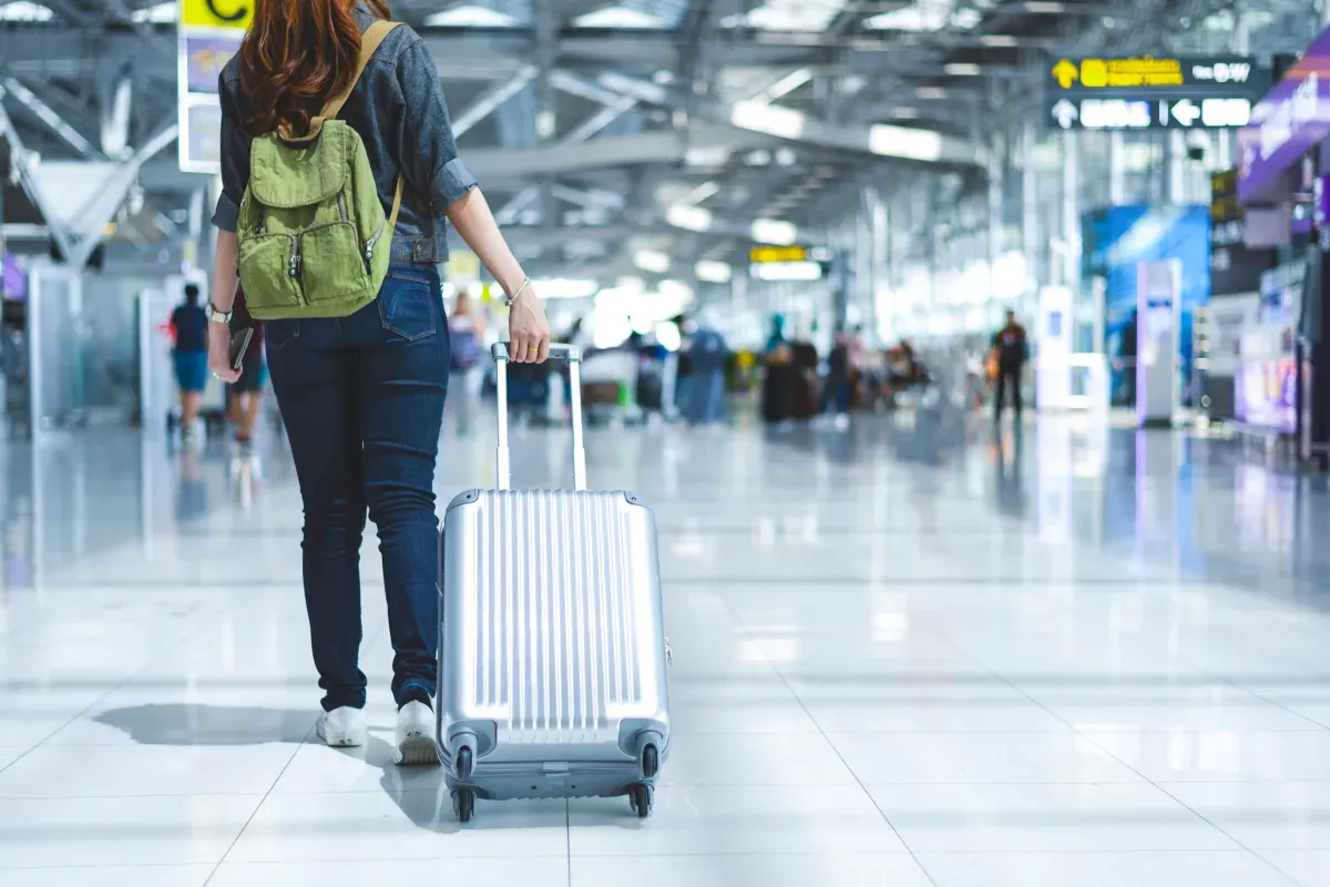 Kobieta z plecakiem i walizką na lotnisku. Zastanawiasz się, ile gotówki można przewieźć samolotem?