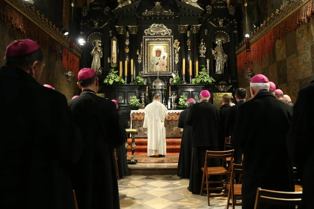 Biskupi w czarnych szatach i różowych biretach modlą się przed obrazem Matki Boskiej na Jasnej Górze, składając intencje mszalne.