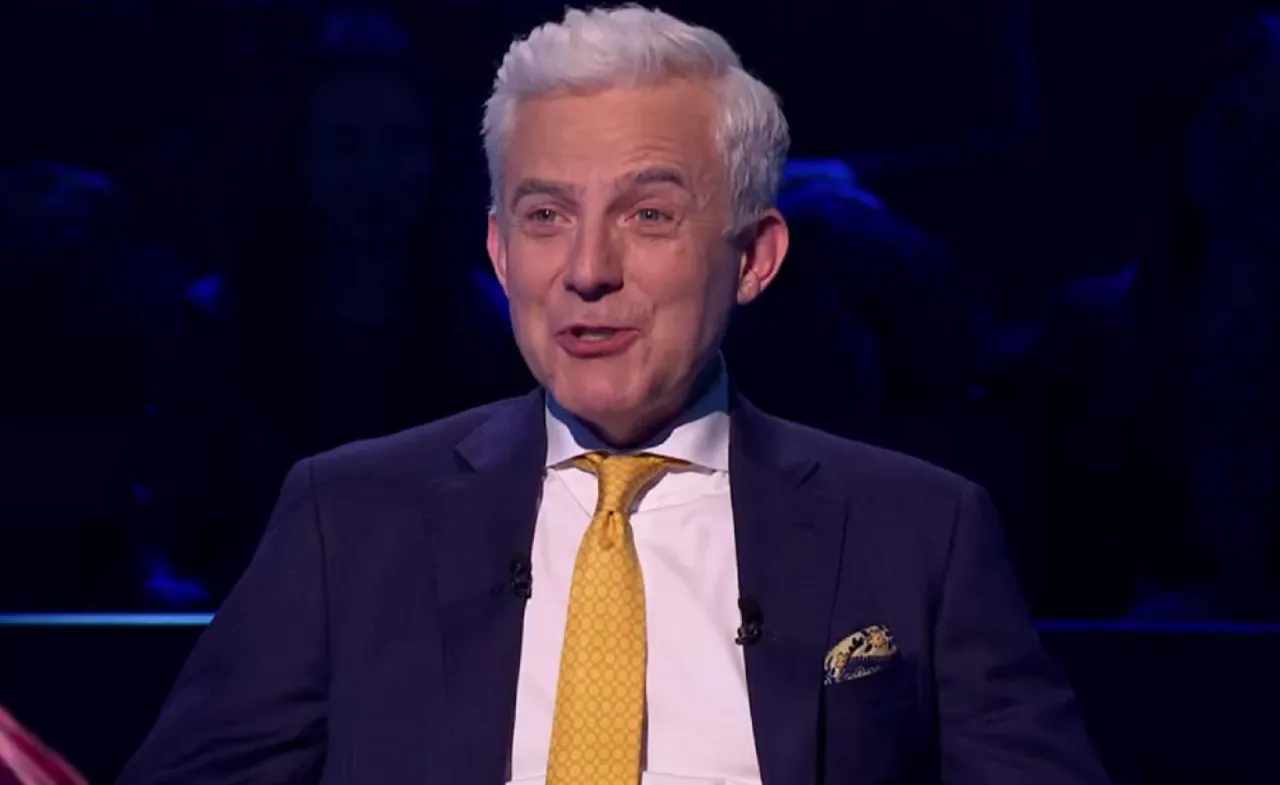 Prowadzący w garniturze z ż&oacute;łtym krawatem, jakby zapowiadał specjalne wydanie 